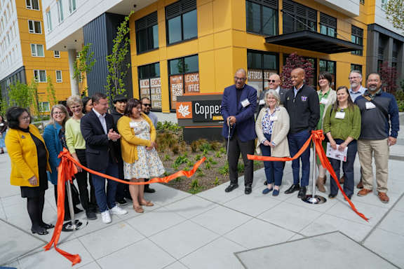 A group of people are gathered in front of a building for a ribbon cutting ceremony.