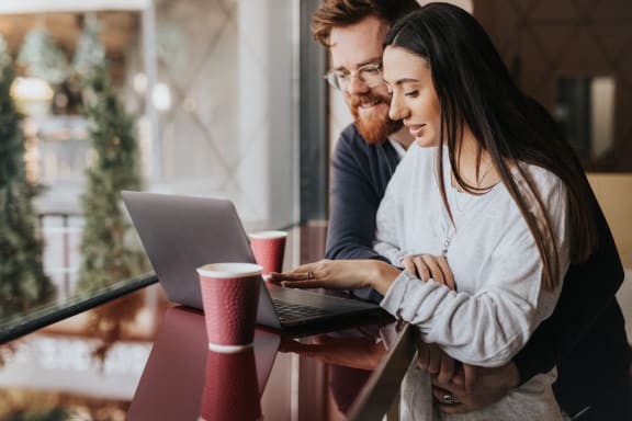 Man and Woman Sitting at Table Looking at Computer Together