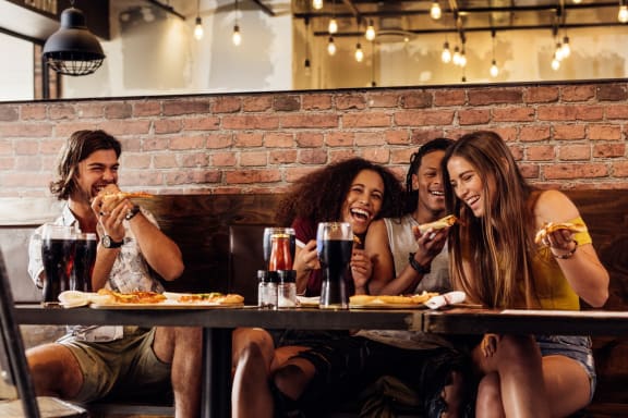 Friends Laughing while Having Pizza and Drinks Together