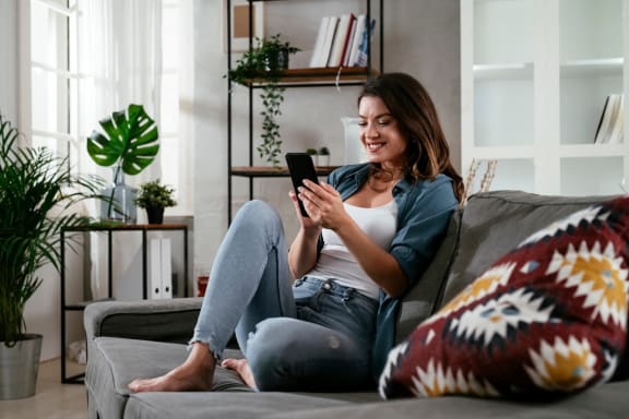 Woman Sitting on Couch Smiling while Looking at Phone