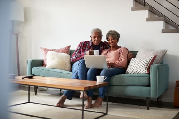 Man and Woman Sitting on Sofa Together Smiling while Looking at Laptop