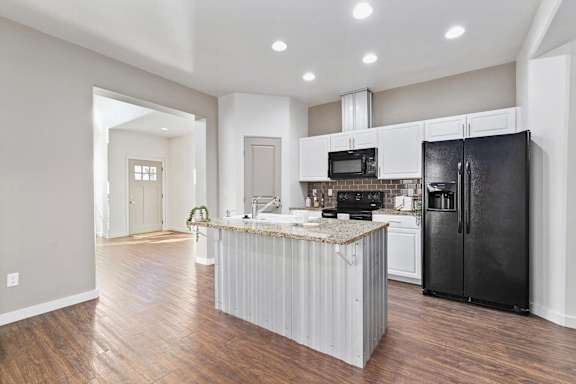 A kitchen with a black refrigerator and a white island.