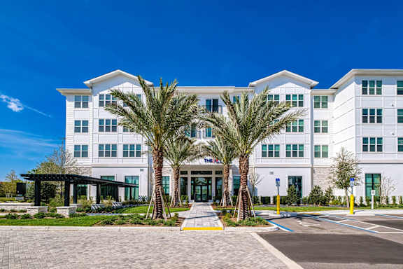 A large white building with a glass entrance and two palm trees in front.