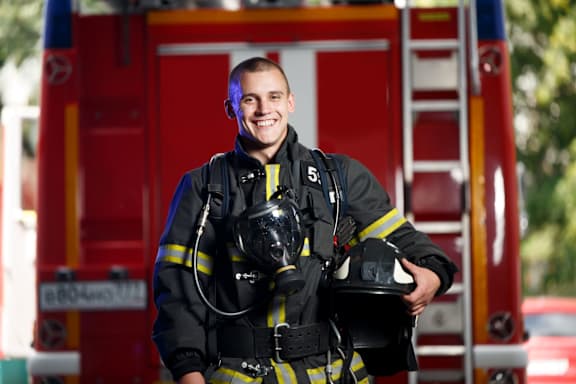 A firefighter in full gear stands in front of a red fire truck.