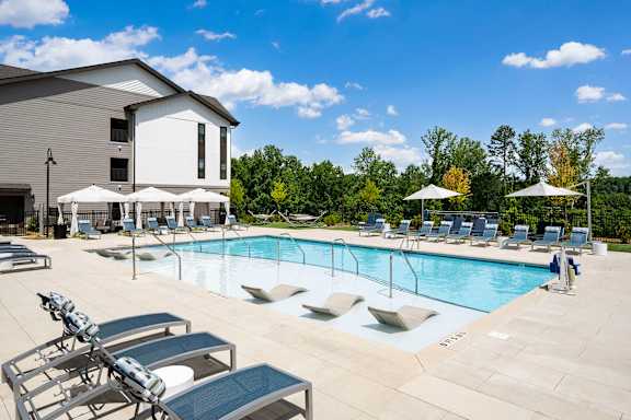 A pool with sun loungers and umbrellas in front of a building.