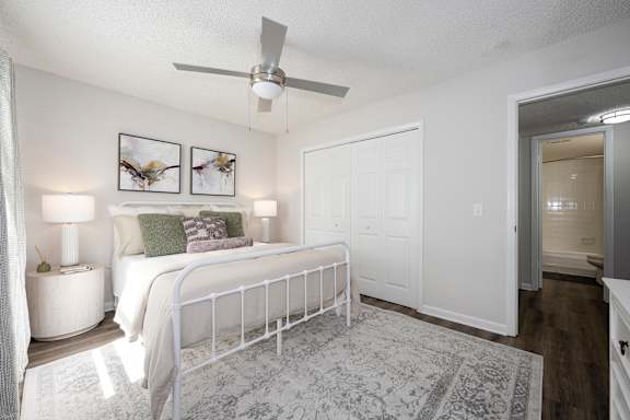 A bedroom with a white bed and a ceiling fan.