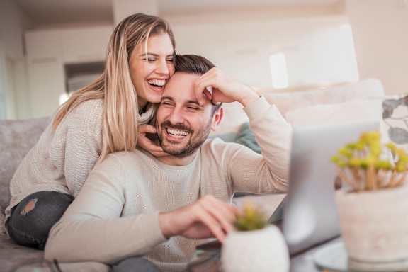 A man and woman are sitting on a couch looking at a laptop screen.
