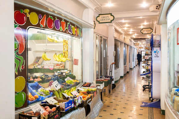 A fruit stand with a sign that says "GREEN GROXERS" is in the middle of a long hallway.