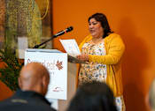 Thumbnail 5 of 16 - A woman is giving a speech at a podium.