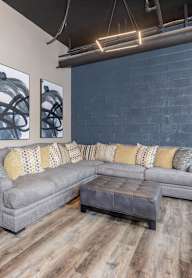 A grey couch with yellow pillows sits in a room with wooden floors.