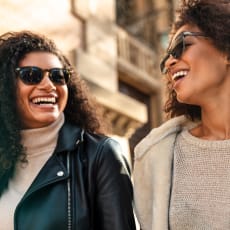 two women walking down the street wearing sunglasses and laughing