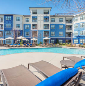 a swimming pool with chaise lounge chairs and umbrellas in front of an apartment building at Streets of Greenbrier in Chesapeake, VA 23320