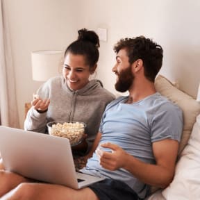 Couple Sitting on Bed Together with Laptop and Popcorn