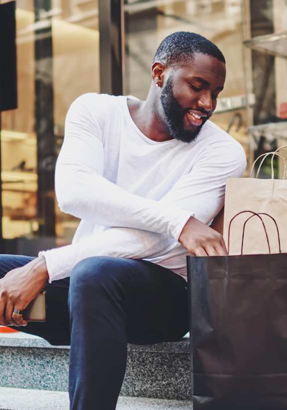 Man Sitting Down Outside Next to Shopping Bags