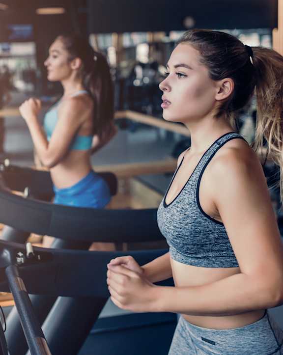 two women running on a treadmill in a gym