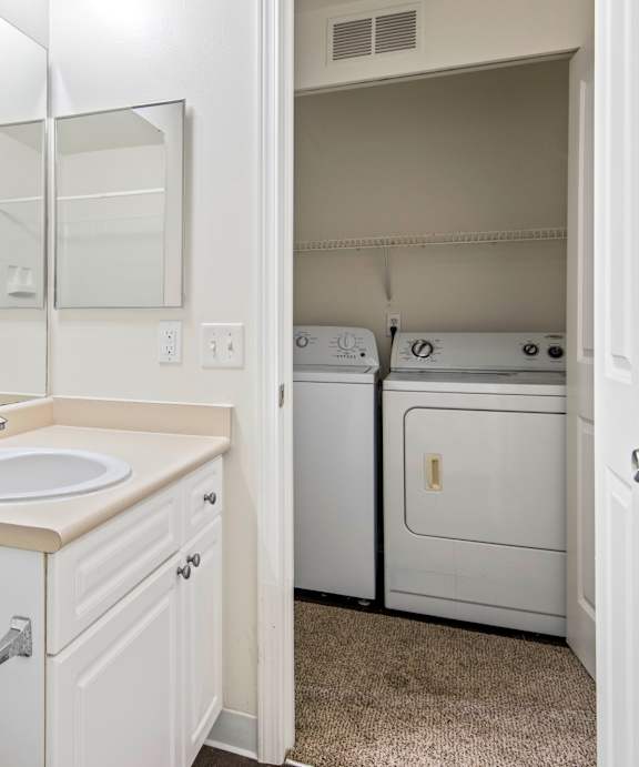 A white bathroom with a sink, mirror, and washer and dryer.