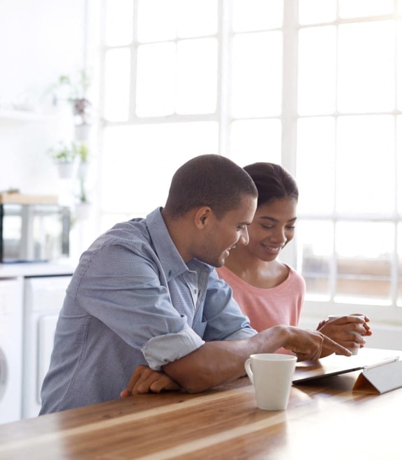 Man and Woman Sitting at Kitchen Counter Together Smiling while Looking at Tablet