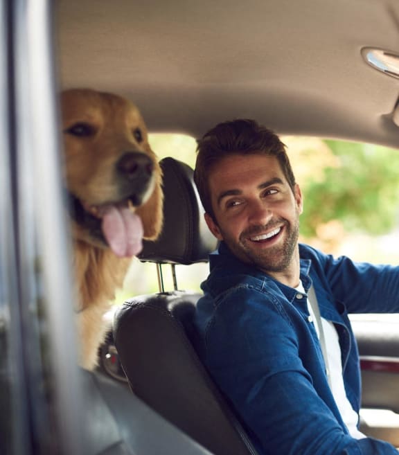Man Smiling while Driving in Car with Dog in Back Seat