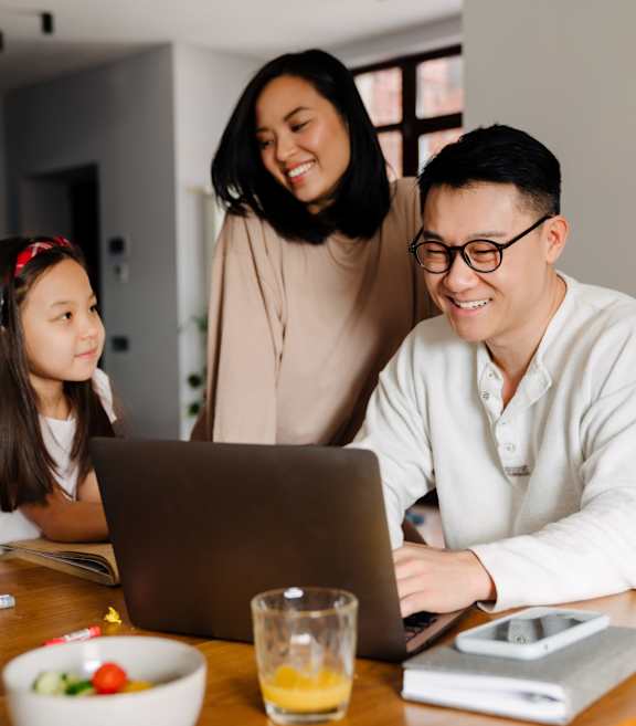 Family Smiling and Sitting at Table Together while Father is on Laptop