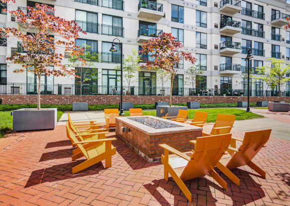A fire pit surrounded by yellow chairs in front of a building.