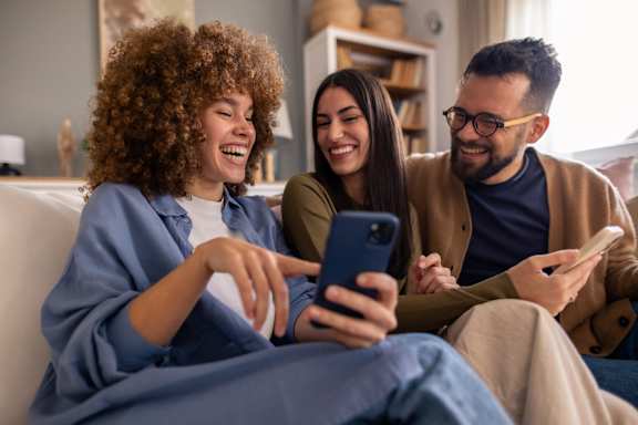 Three people are sitting on a couch, looking at a smartphone.