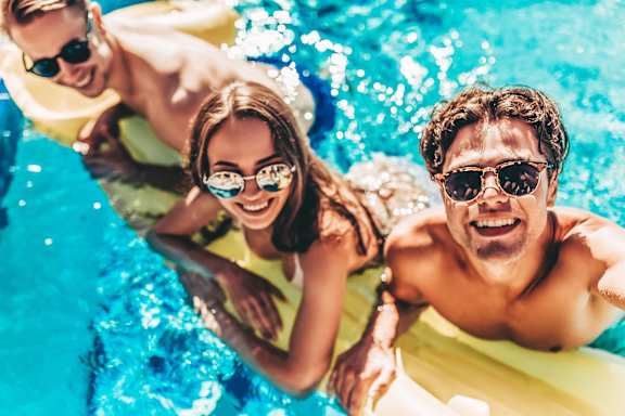 Three people are enjoying a sunny day in a pool.