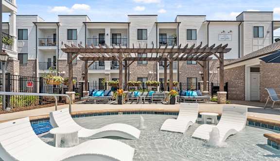 A pool area with a wooden pergola and lounge chairs.