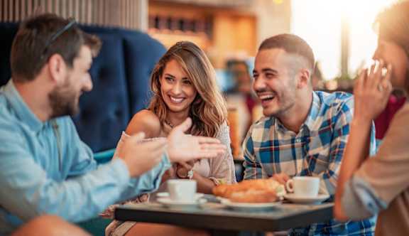 A group of people are sitting around a table taking a selfie.