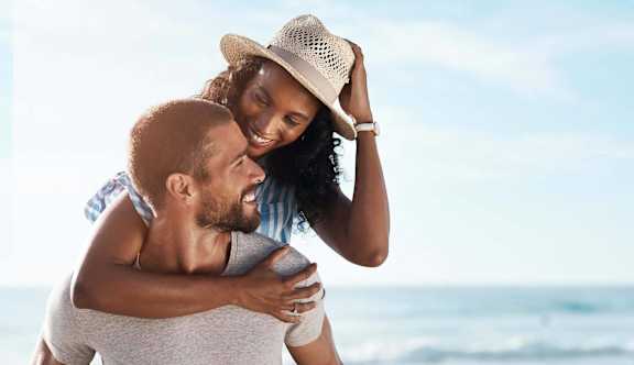 man carrying woman on his back on the beach