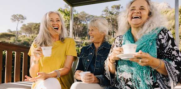Women Laughing and Sitting on Bench Drinking Coffee Together