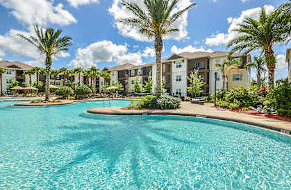 a swimming pool with palm trees in front of an apartment complex at Cabana Club Apartments in Jacksonville