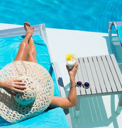 A woman in a straw hat is relaxing by the pool with a drink.