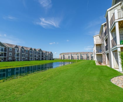 a large grassy field next to a body of water in front of some apartments