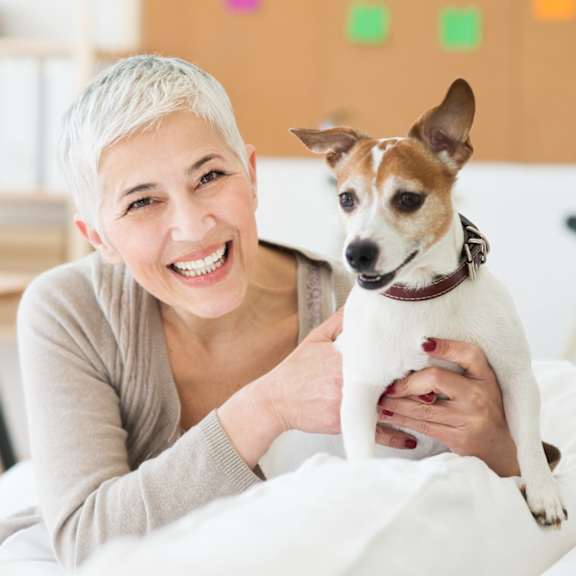 A woman with short hair is holding a small dog with a white and brown coat.