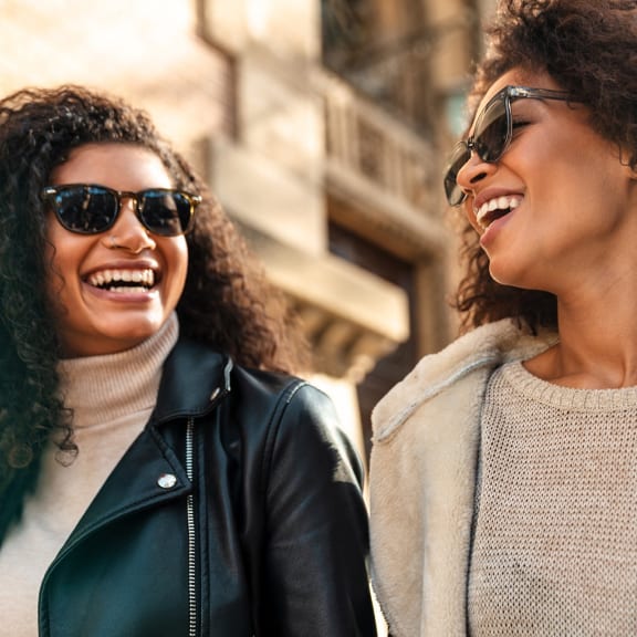 two women walking down the street wearing sunglasses and laughing