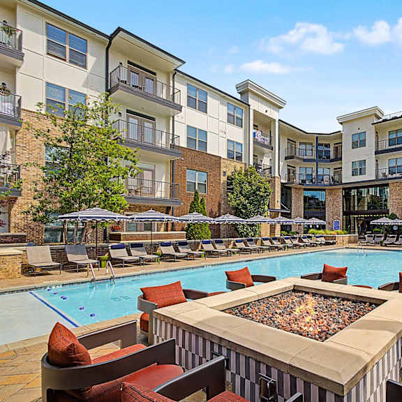 A large outdoor pool surrounded by a fire pit and lounge chairs.