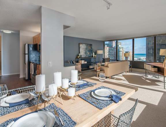A dining table set with plates and candles in a room with a view of the city.