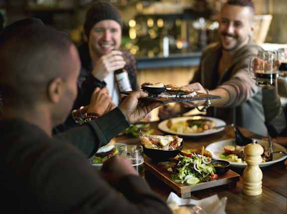 Friends Sitting Around Table Smiling and Having Food and Drinks Together