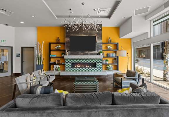 A modern living room with a grey sofa and a television on a yellow wall.