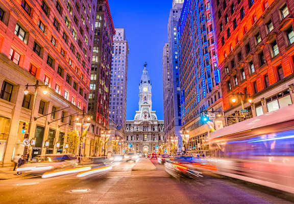 A city street at night with cars passing by and a tall building in the background.