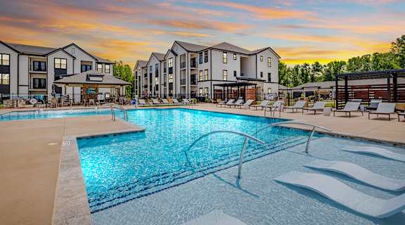 A swimming pool in front of apartment buildings at sunset.