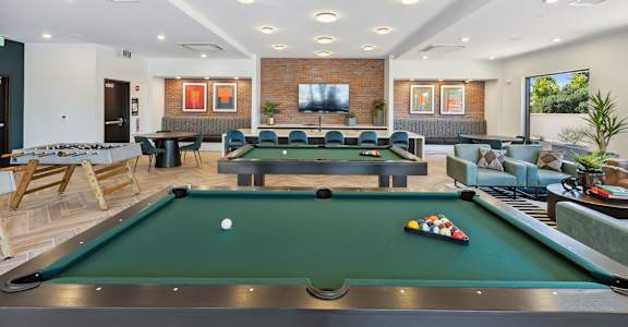 A pool table is in the middle of a room with a couch and a television.