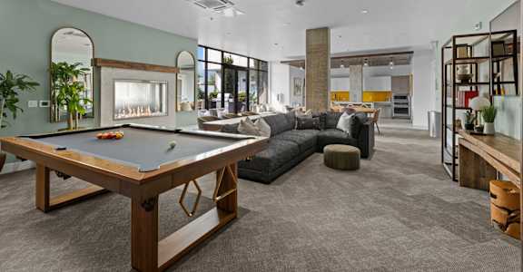 A billiard table is in the middle of a room with a couch and a mirror.