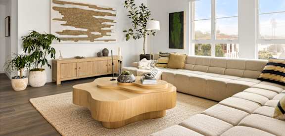 A living room with a large couch, a coffee table, and a wooden wall art.