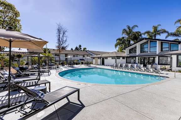 A pool area with sun loungers and a building in the background.