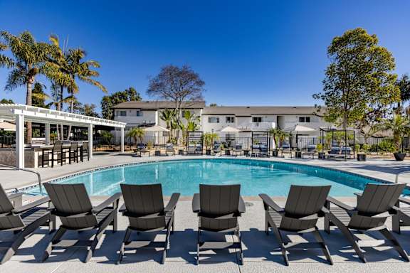 A pool surrounded by chairs and trees.