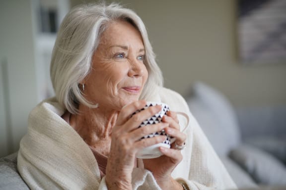 an older woman sitting on a couch holding a cup of coffee