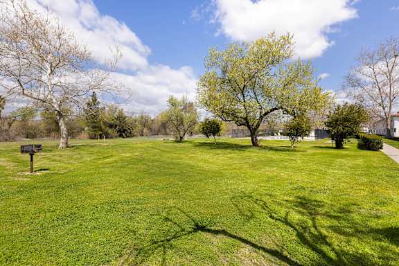 A green grassy field with trees and a sign in the distance.