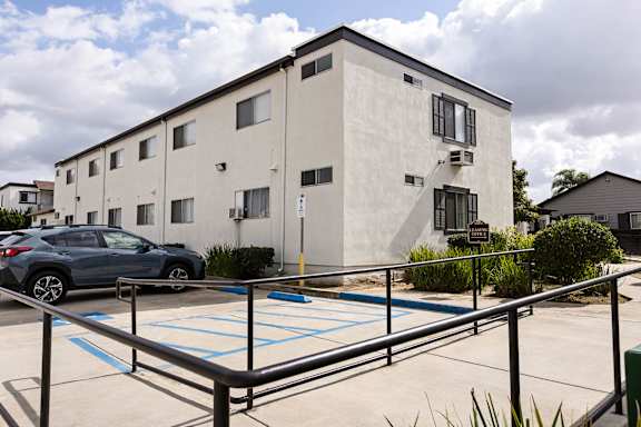 A parking lot in front of a white building with a blue car parked in the spot.