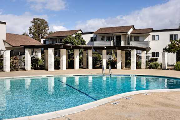 A swimming pool in front of a house with a white fence.
